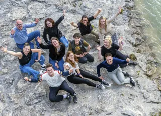 Eine Gruppe Journalist*innen von der katholischen Journalismusschule ifp sitzt am Ufer der Isar in München. 